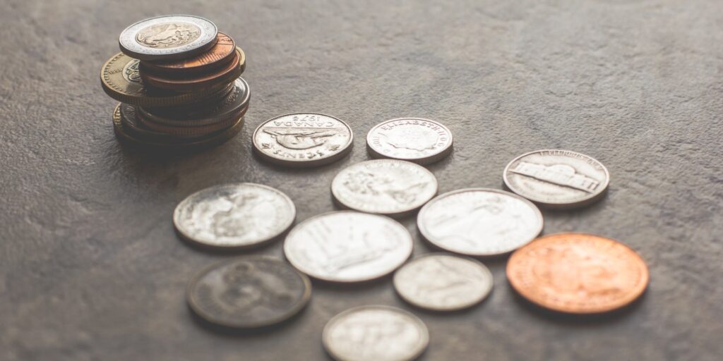 Loose coins on a gray surface including a stack of coins in the background