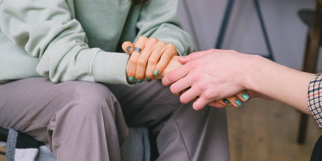 View of two pairs of hands, with one person comforting the other. 