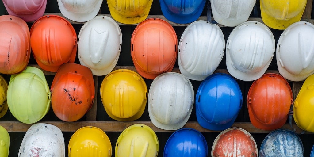 Different coloured hard hats hanging on a wall in rows