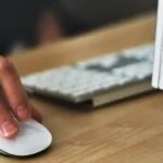 Close up of hand on computer mouse by a computer and keyboard