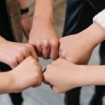 Five hands fist pumping each other in a circle of support