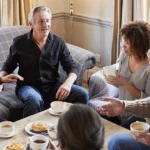 Group of middle aged friends sitting in a living room and chatting over coffee and pastries