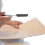 A person's hand extending a pen to another person to sign a document