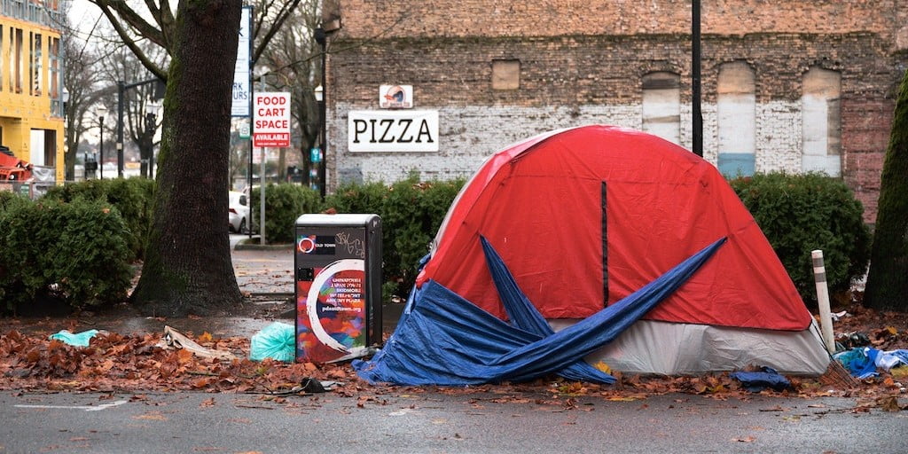 Tent on side of street and in front of brick building in an urban centre.