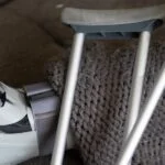 Close up of leg in walking cast, partially covered in a blanket, with crutches laying on top.