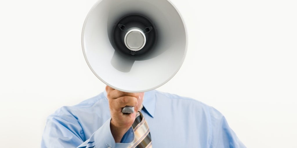 Person in dress shirt and tie holding a megaphone covering their face