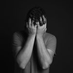 Black and white photo of a person holding their face in their hands in despair.