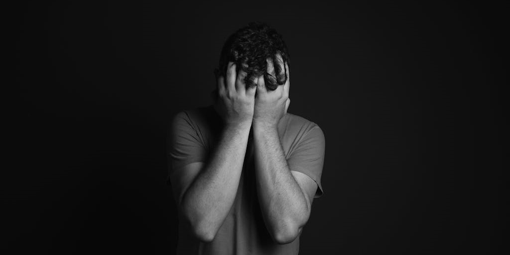 Black and white photo of a person holding their face in their hands in despair.
