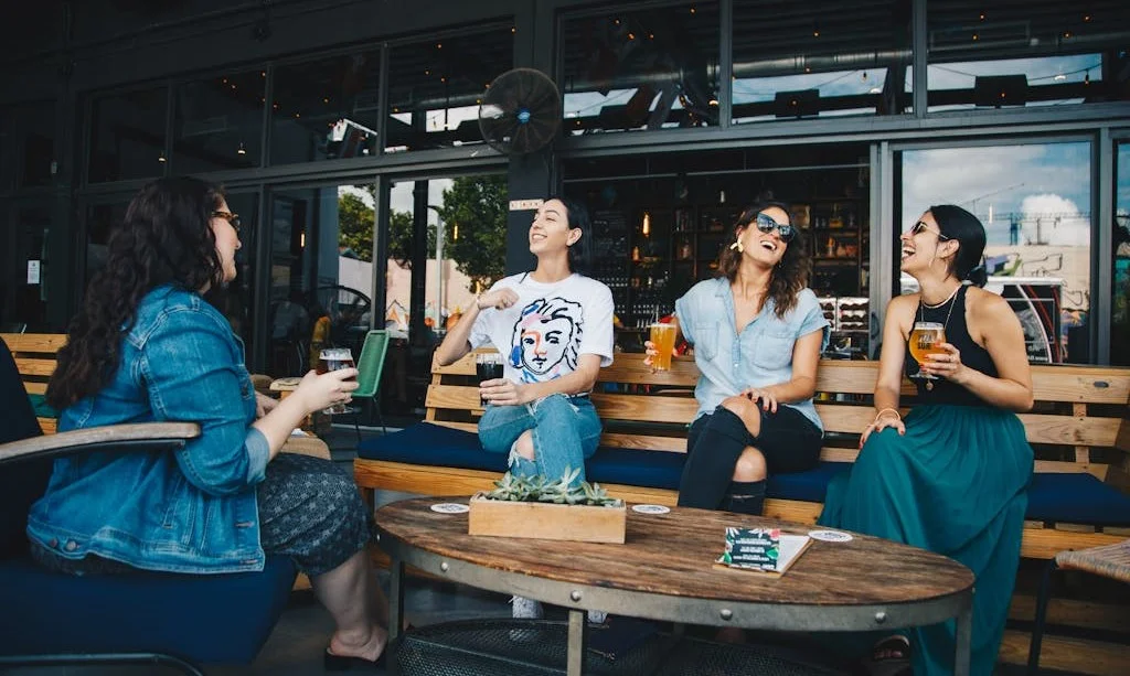 Four young women sitting outside at a cafe chatting. laughing and drinking beverages.