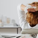 Woman facing away from the camera, sitting in an office chair with her hands behind her head holding a tissue