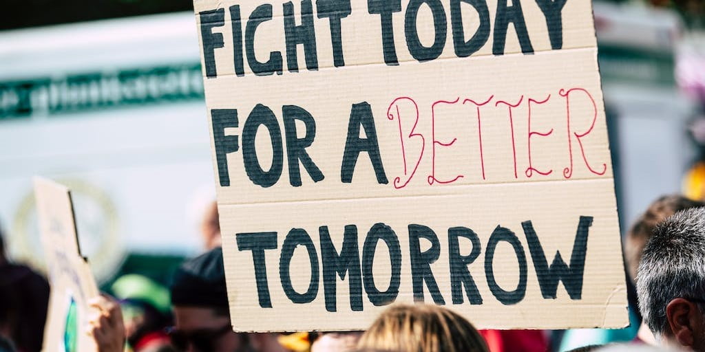 Cardboard sign being held in a crowd with the text "Fight for a better tomorrow" painted on it.