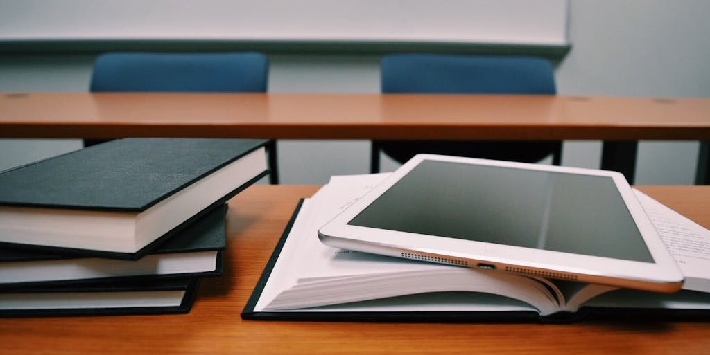 Textbooks piled on a desk beside with an open textbook with a tablet on top