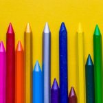 Several pencil crayons in different colours lined up against a yellow background