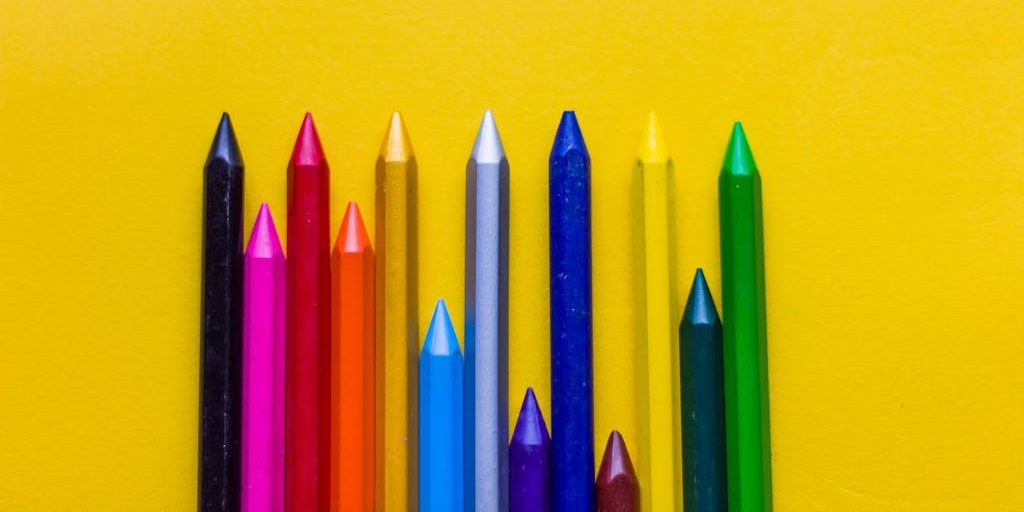 Several pencil crayons in different colours lined up against a yellow background