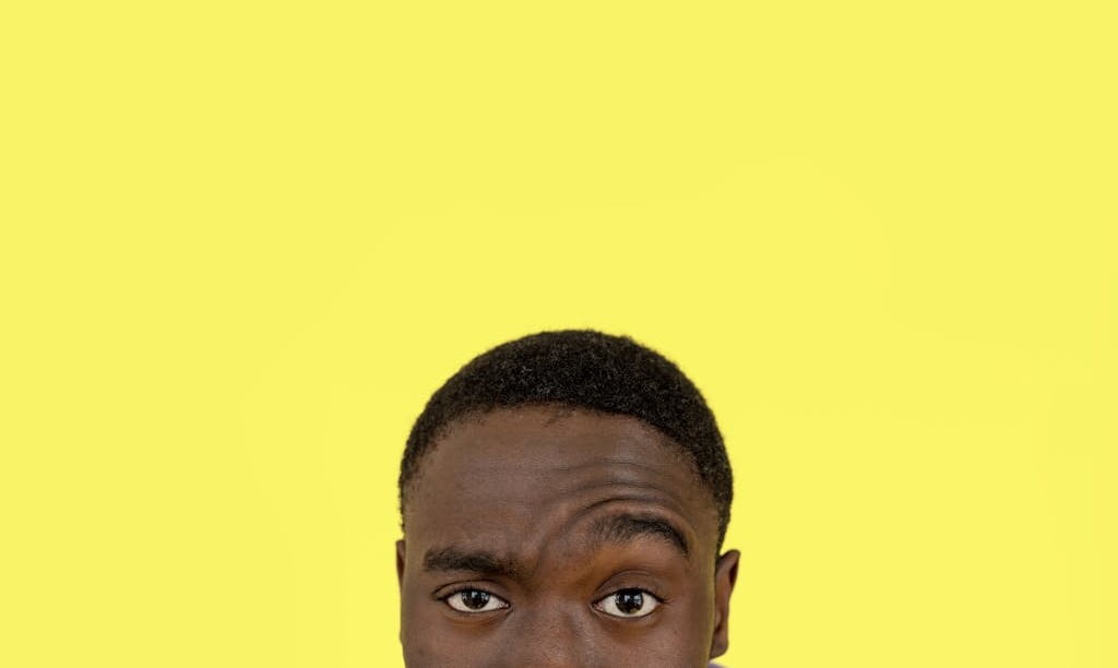 View of man's face from nose up against a yellow background. The man has one eyebrow raised, questioningly.