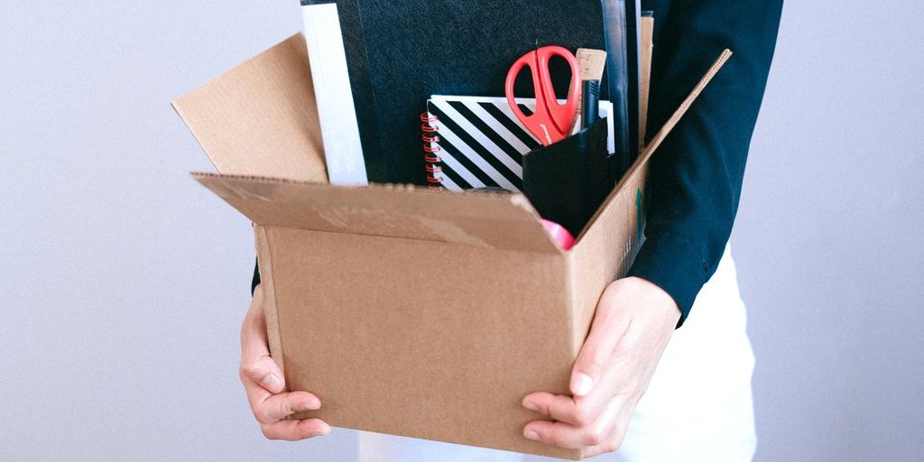 Woman carrying cardboard box with office items